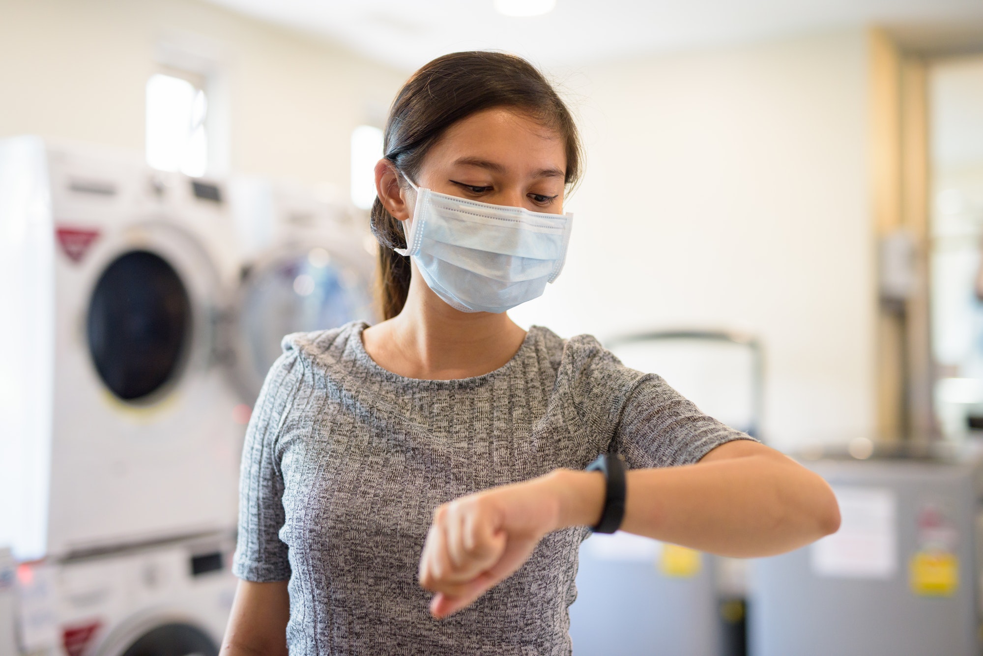 Young Asian woman with mask checking the time at the laundromat